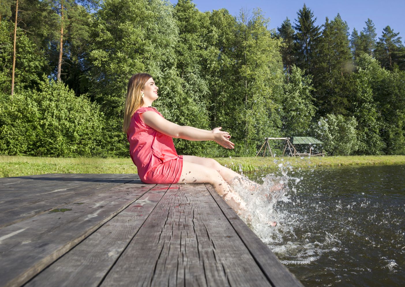 Junge Frau auf einem Steg sitzend sprudelt Wasser mit den Beinen 